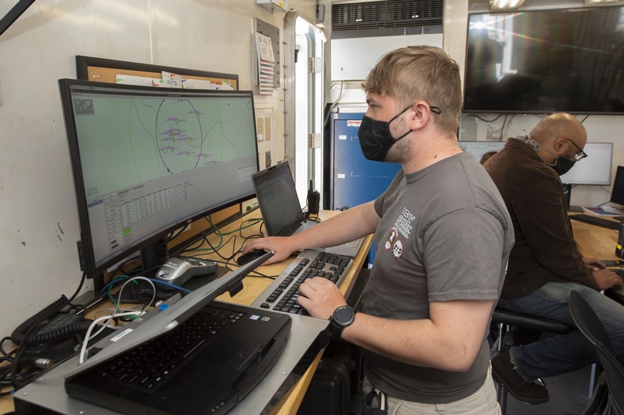 Dois operadores da Marinha dos EUA trabalham em estações de computador usadas no preparo dos navios não tripulados Sea Hunter e Sea Hawk.