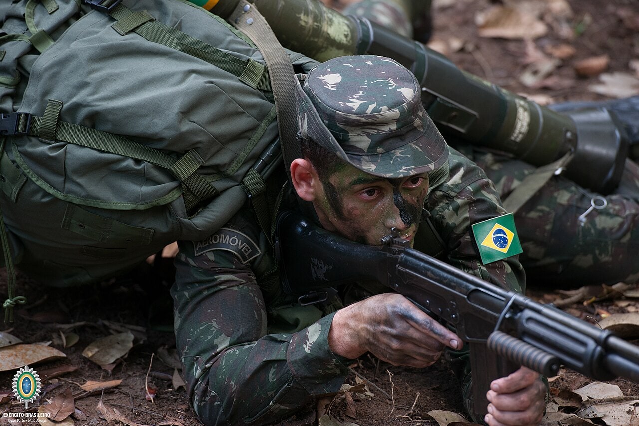 Militar brasileiro camuflado rasteja no chão da floresta com fuzil e mochila de campanha