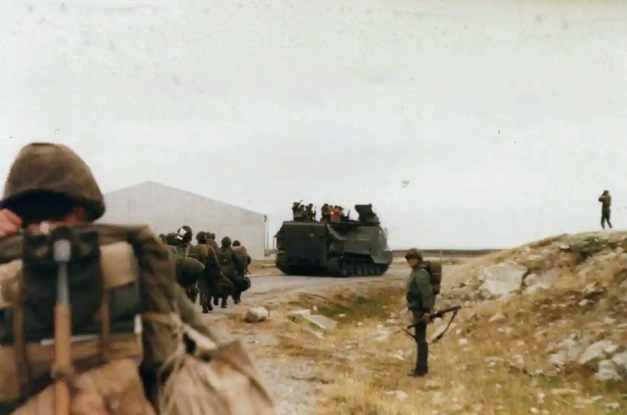 Militares argentinos caminham em direção a um veículo blindado sobre terreno pedregoso, com mochilas e fuzis.