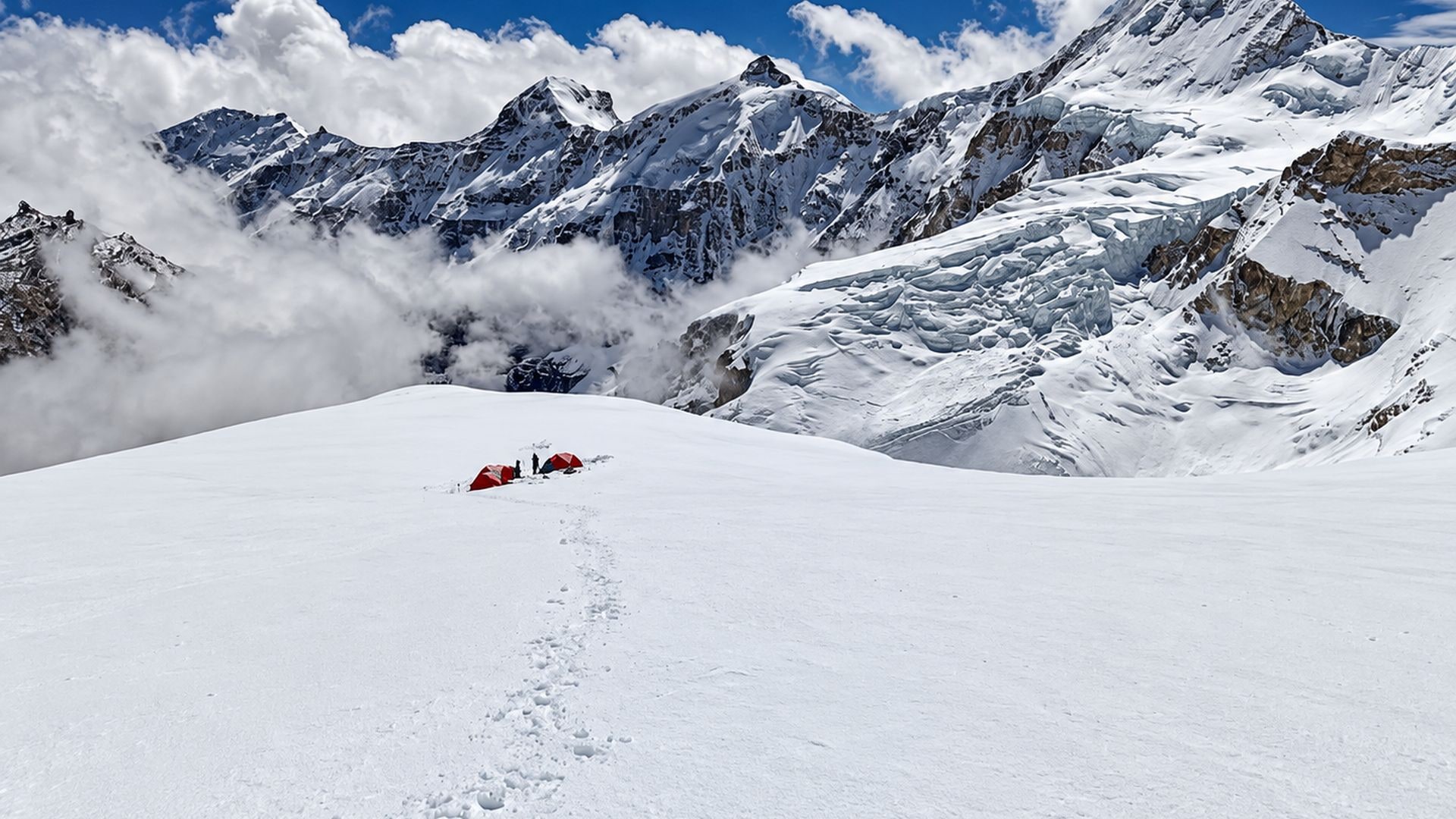 Acampamento de alta montanha montado sobre terreno nevado no Himalaia, com barracas e picos cobertos de neve ao fundo.